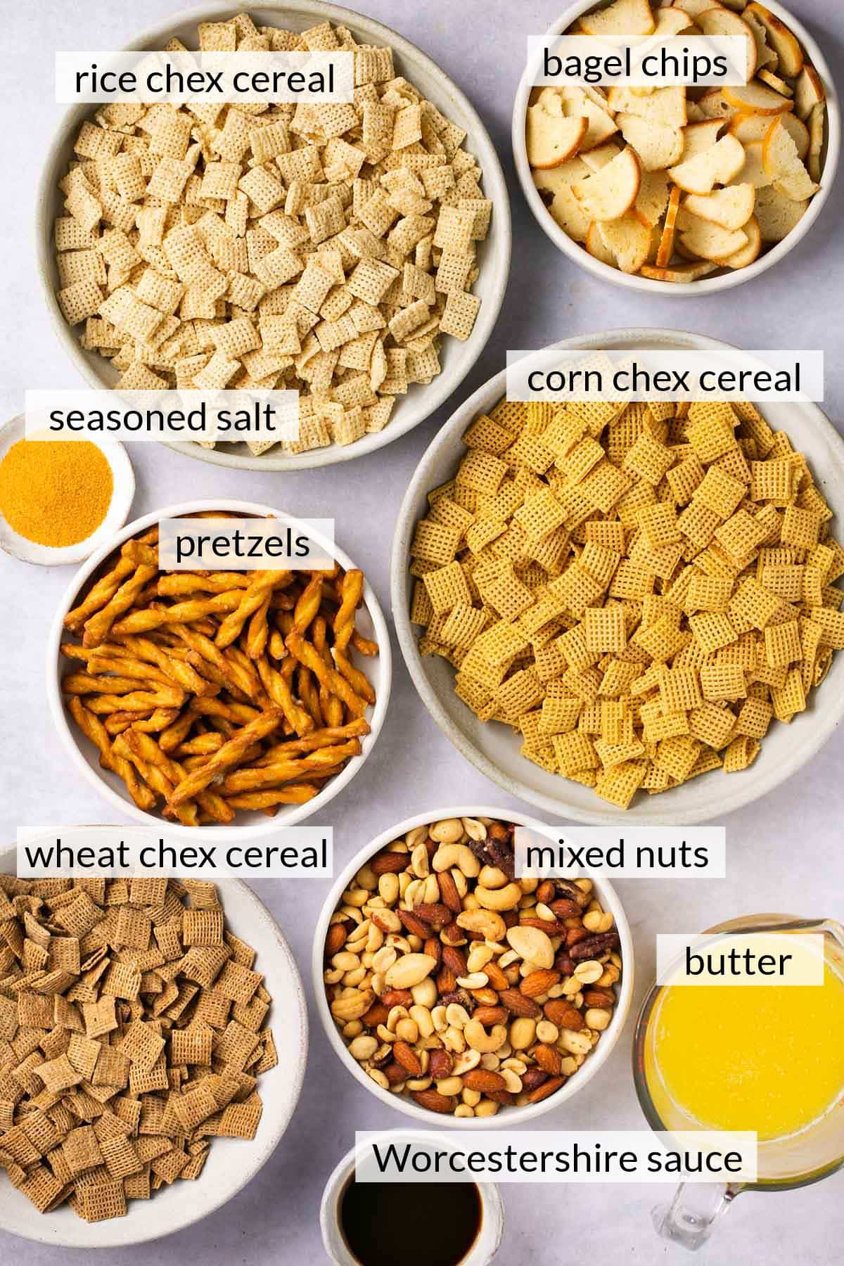 Chex cereal, pretzels, bagel chips, melted butter, mixed nuts and seasoned salt divided into bowls.