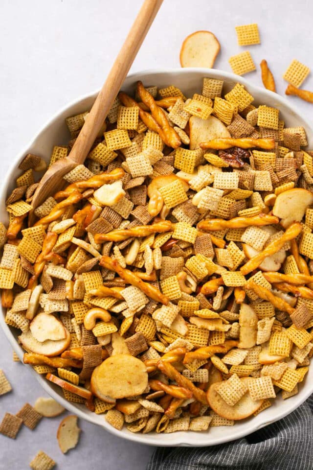 Chex snack mix in a large white bowl with a wooden spoon.
