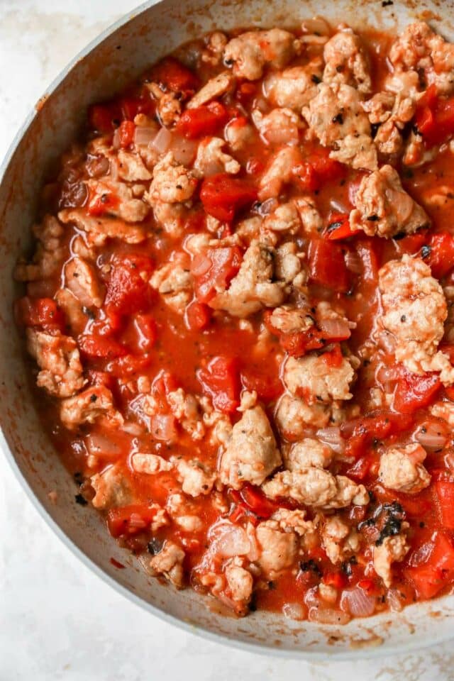 Meat, tomatoes and seasoning cooking in a pan.