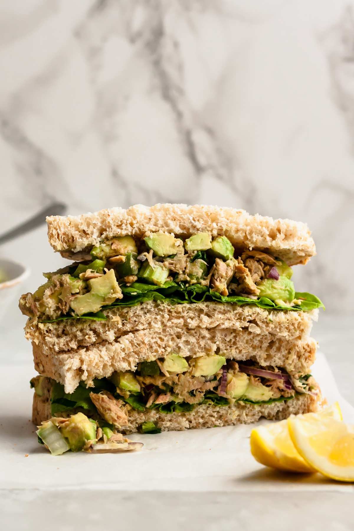 Sandwich made with avocado tuna salad near lemon wedges.