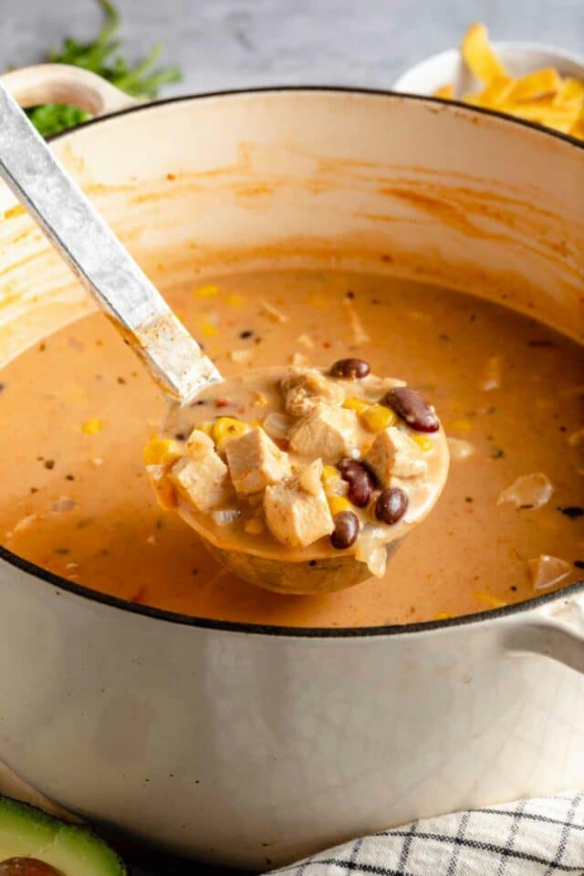 Using a ladle to serve creamy chicken tortilla soup out of a large pot.