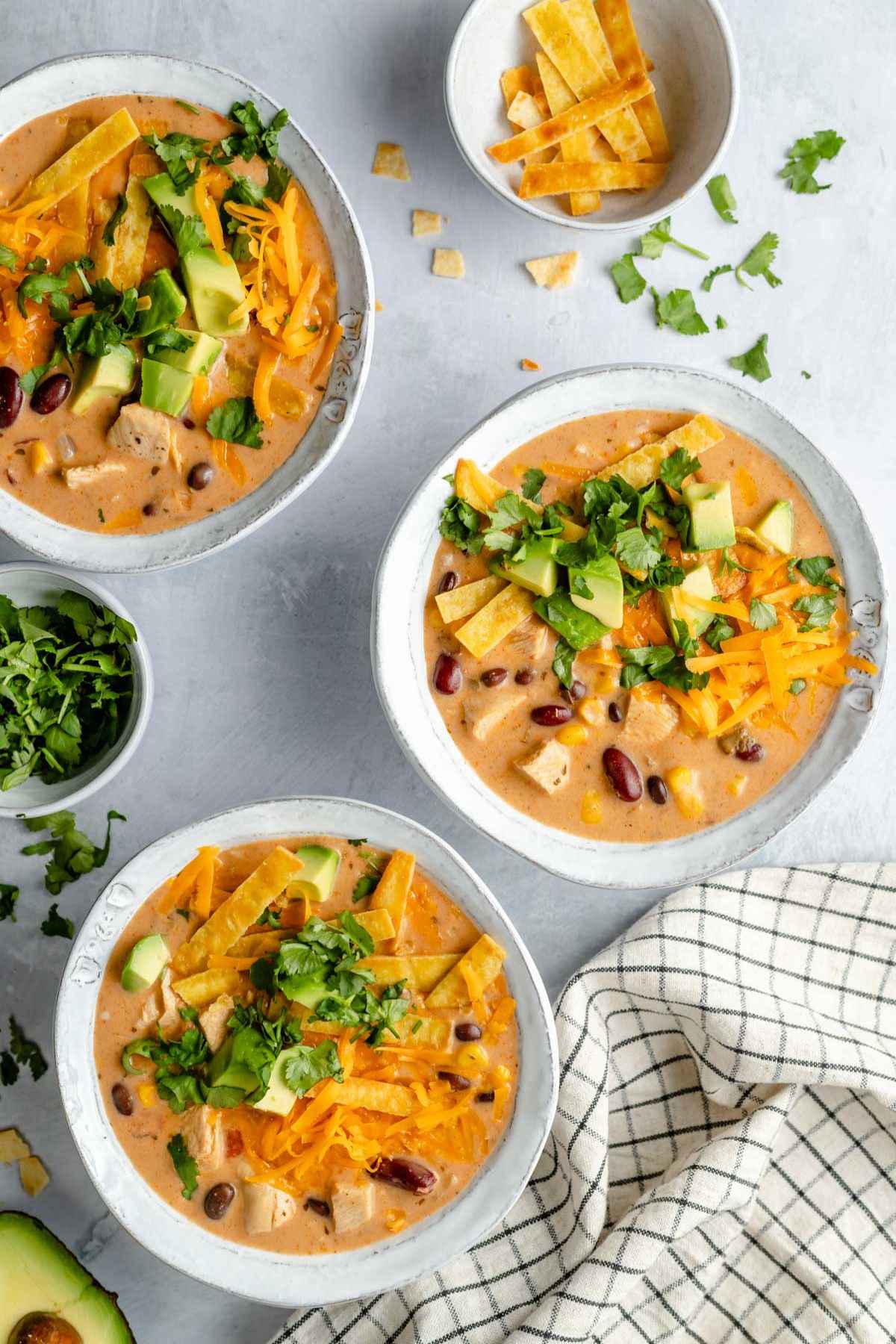 White bowls with a chicken soup topped with cilantro and avocado.
