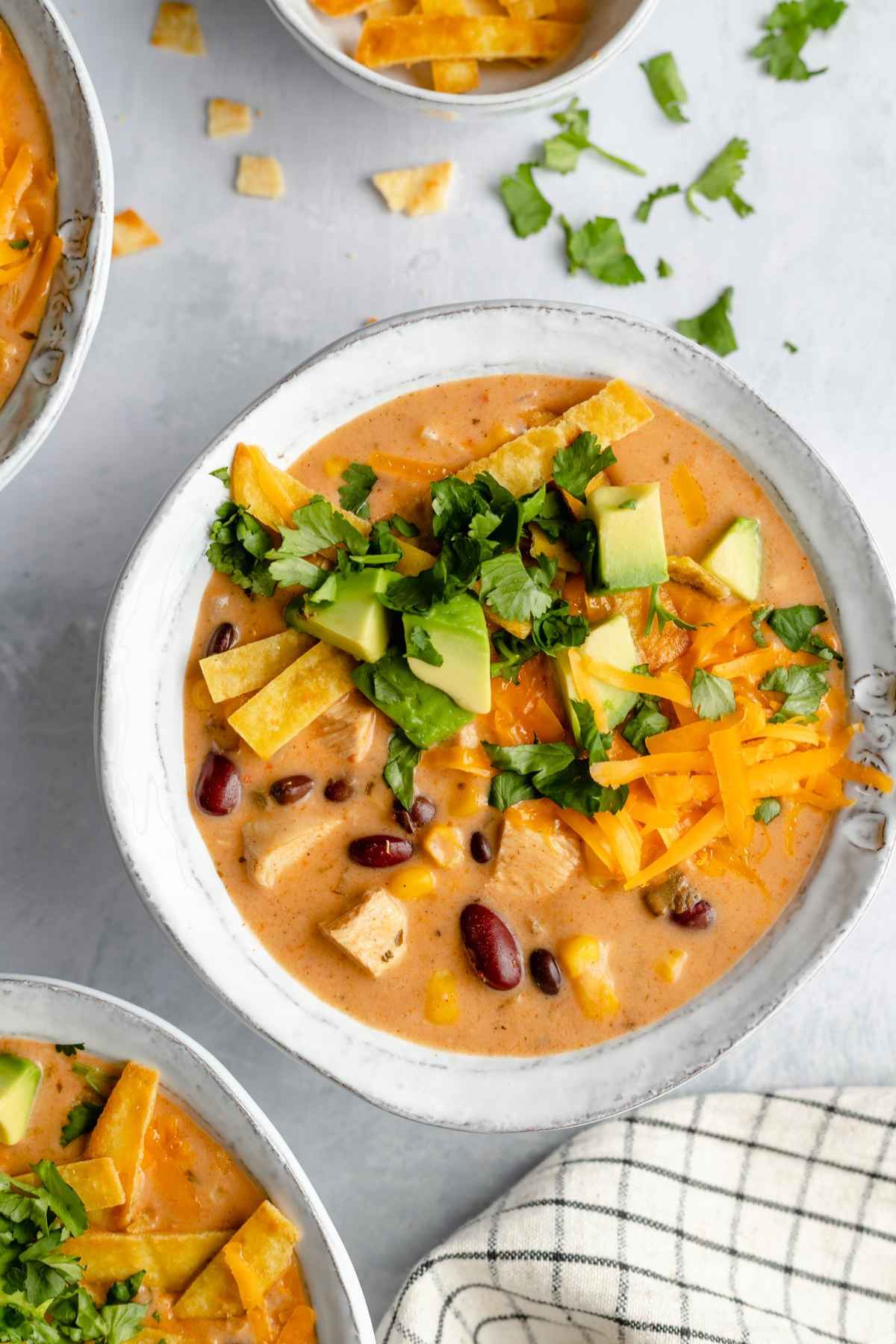 Bowl of creamy chicken soup topped with cheese, cilantro and avocado.