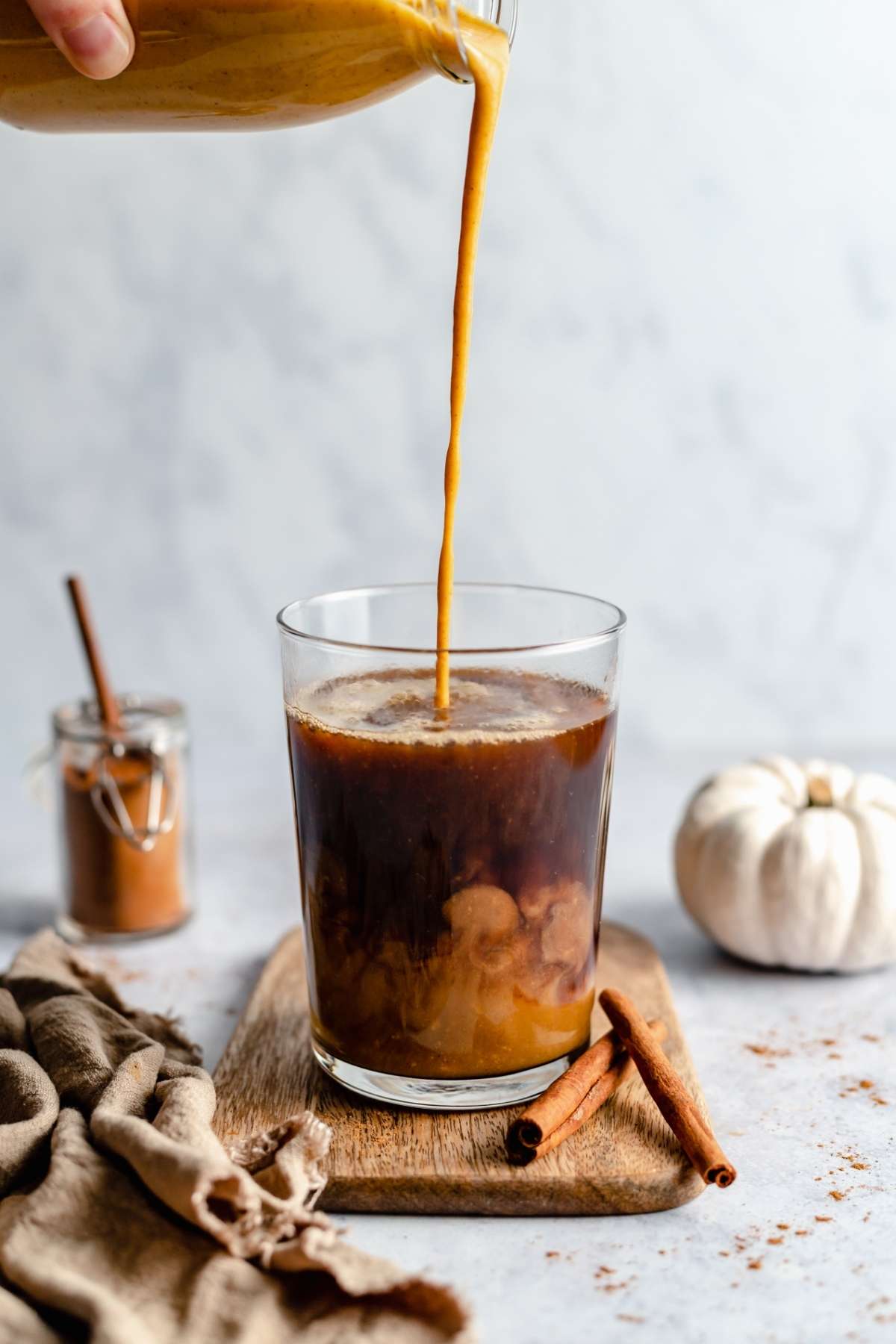 Pouring pumpkin creamer into a glass with coffee.