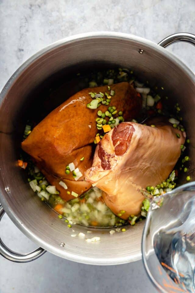 Adding ham hocks to a large soup pot.