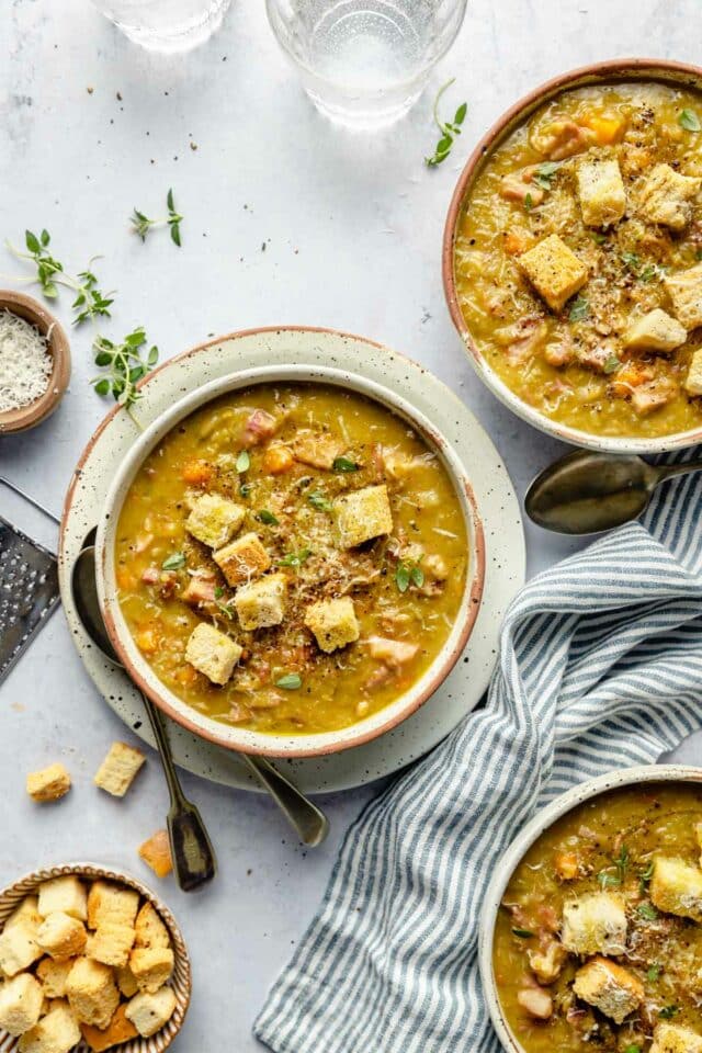 Bowls of split pea soup topped with croutons and fresh thyme leaves.