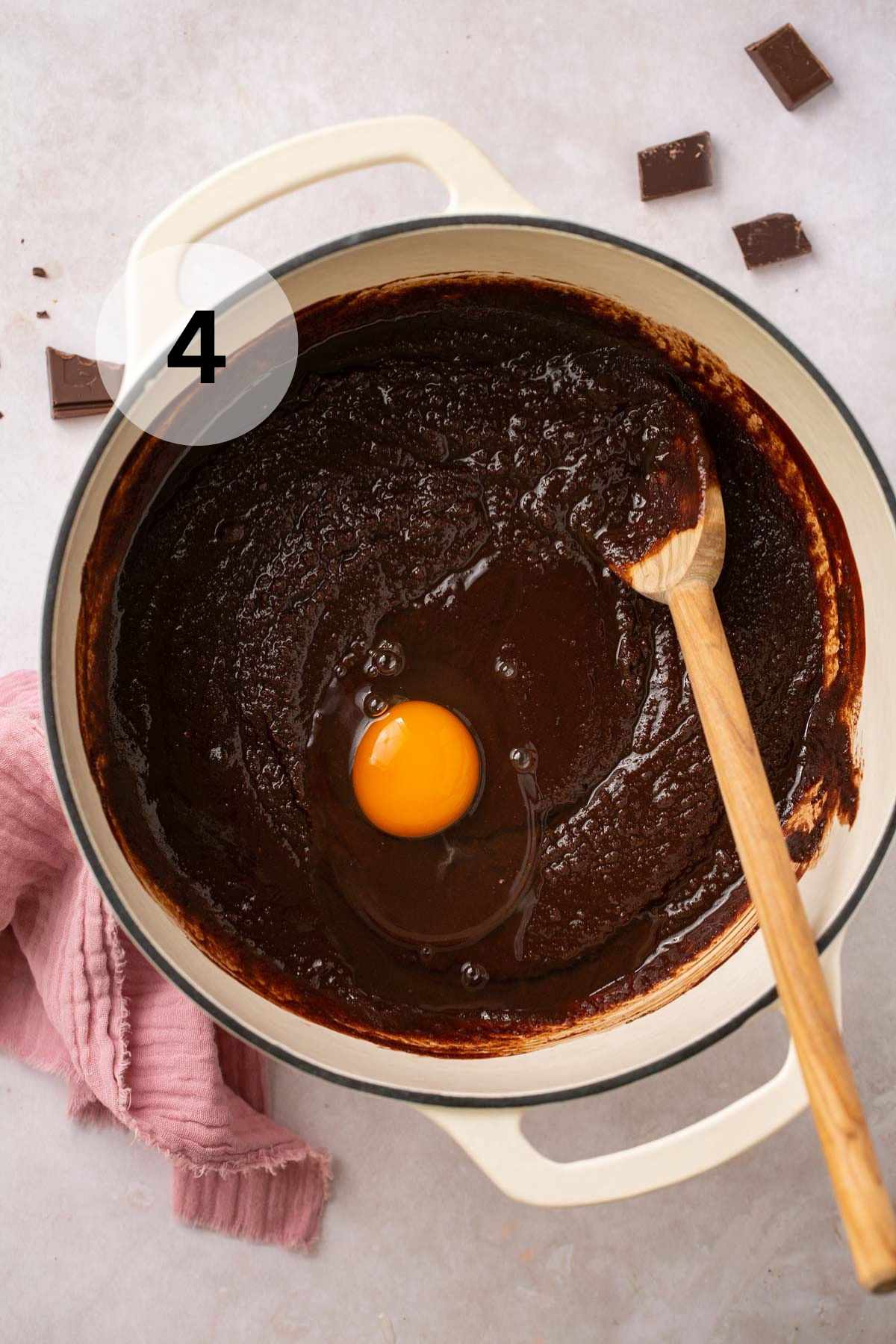An egg cracked over brownie batter in a large pot.
