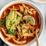 Slow cooker chicken tortilla soup in a white bowl with a spoon.