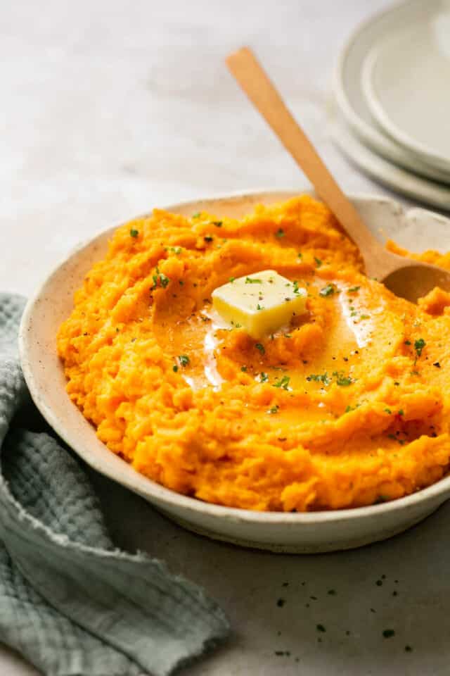 Mashed sweet potatoes in a bowl with a wooden spoon.