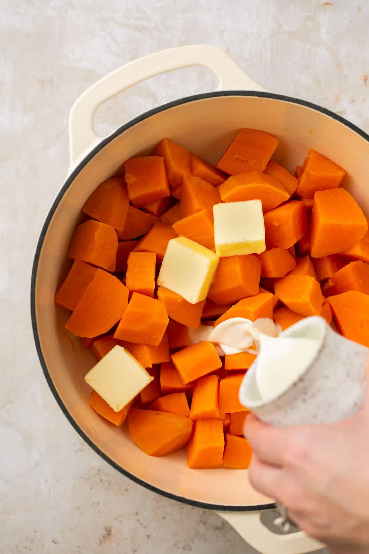 Pouring cream into cubed sweet potatoes.