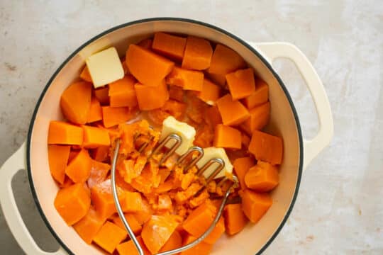 Using a metal masher to mash butter and cream into sweet potatoes.