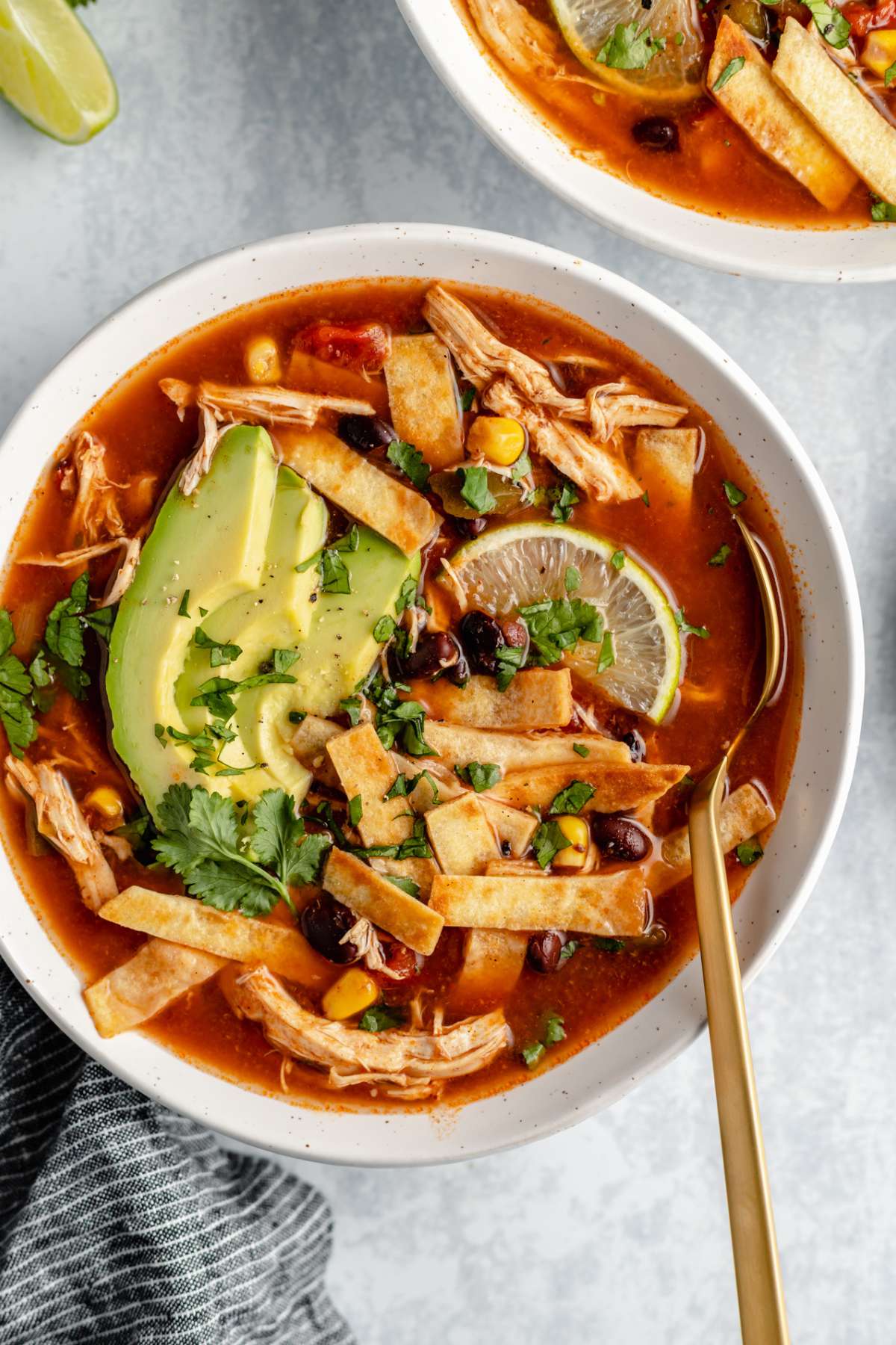 Slow cooker chicken tortilla soup in a white bowl with a spoon.