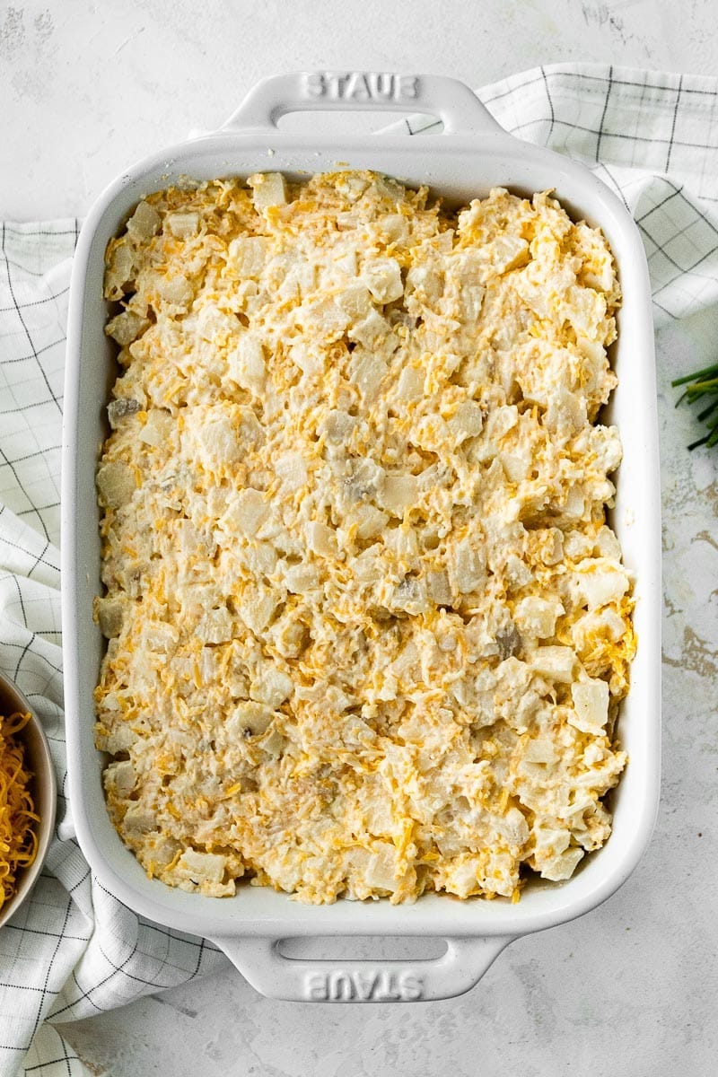 Adding potato casserole to a large baking dish.