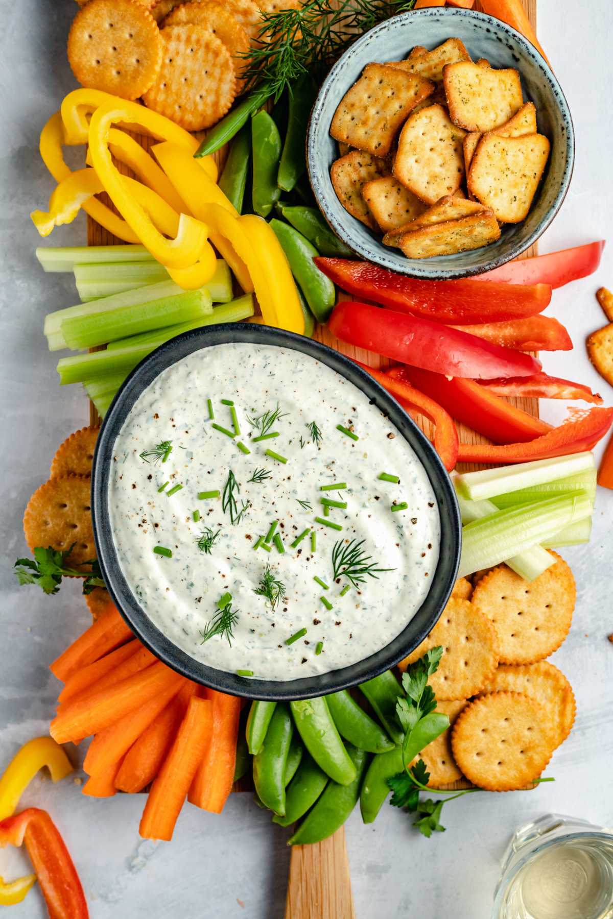 Crackers and fresh vegetables on a serving board with cream cheese dip.