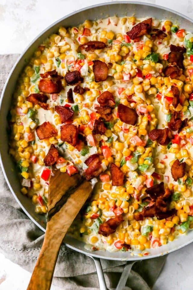 Stirring creamed corn topped with bacon in a pan.