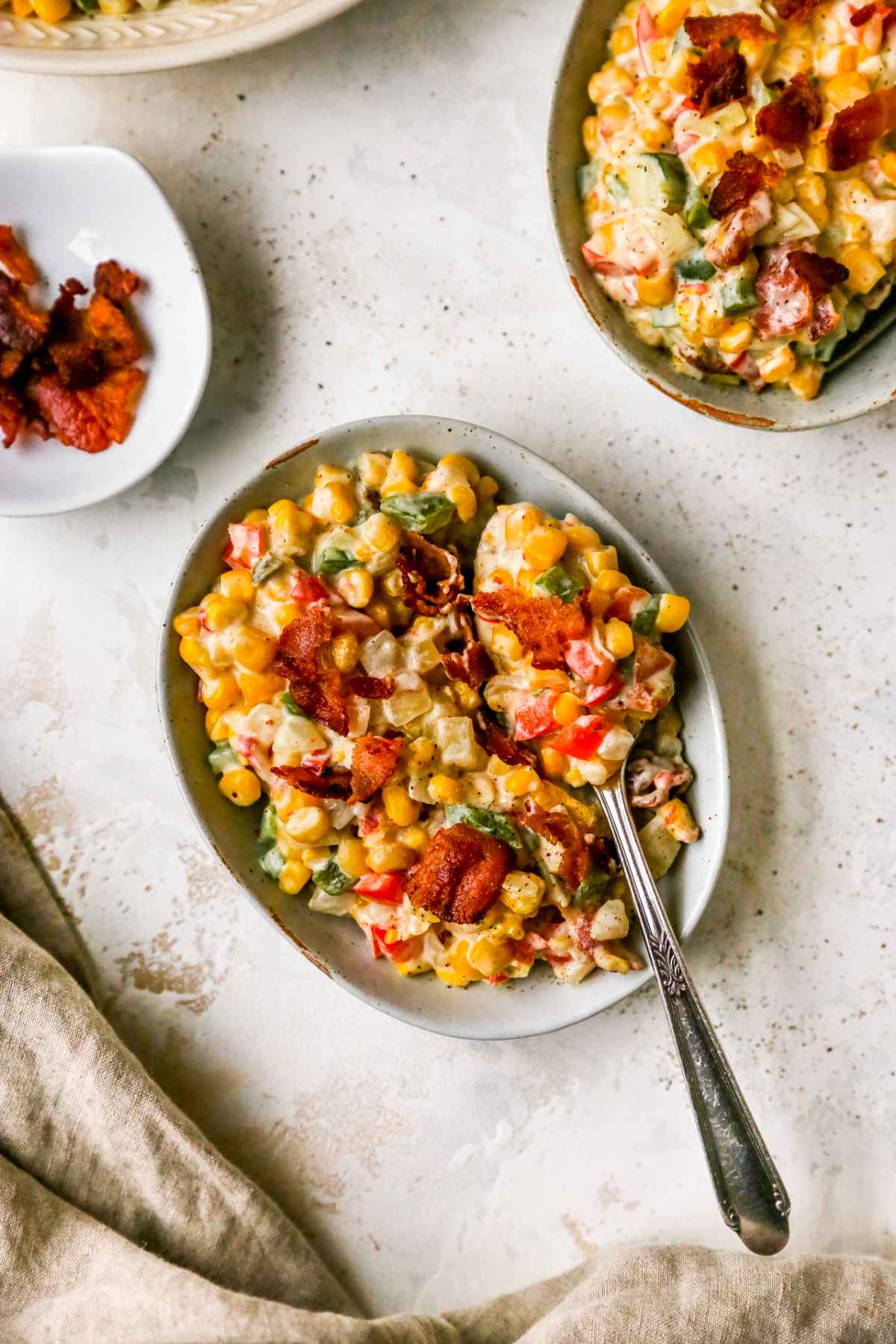 Creamy corn with bacon and bell pepper in a small bowl with a spoon.
