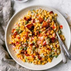 Creamed corn topped with crumbled bacon on a plate with a fork.