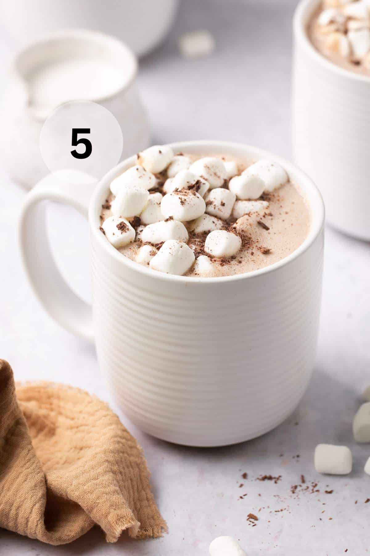 Hot cocoa topped with marshmallows and cocoa powder in a white mug.