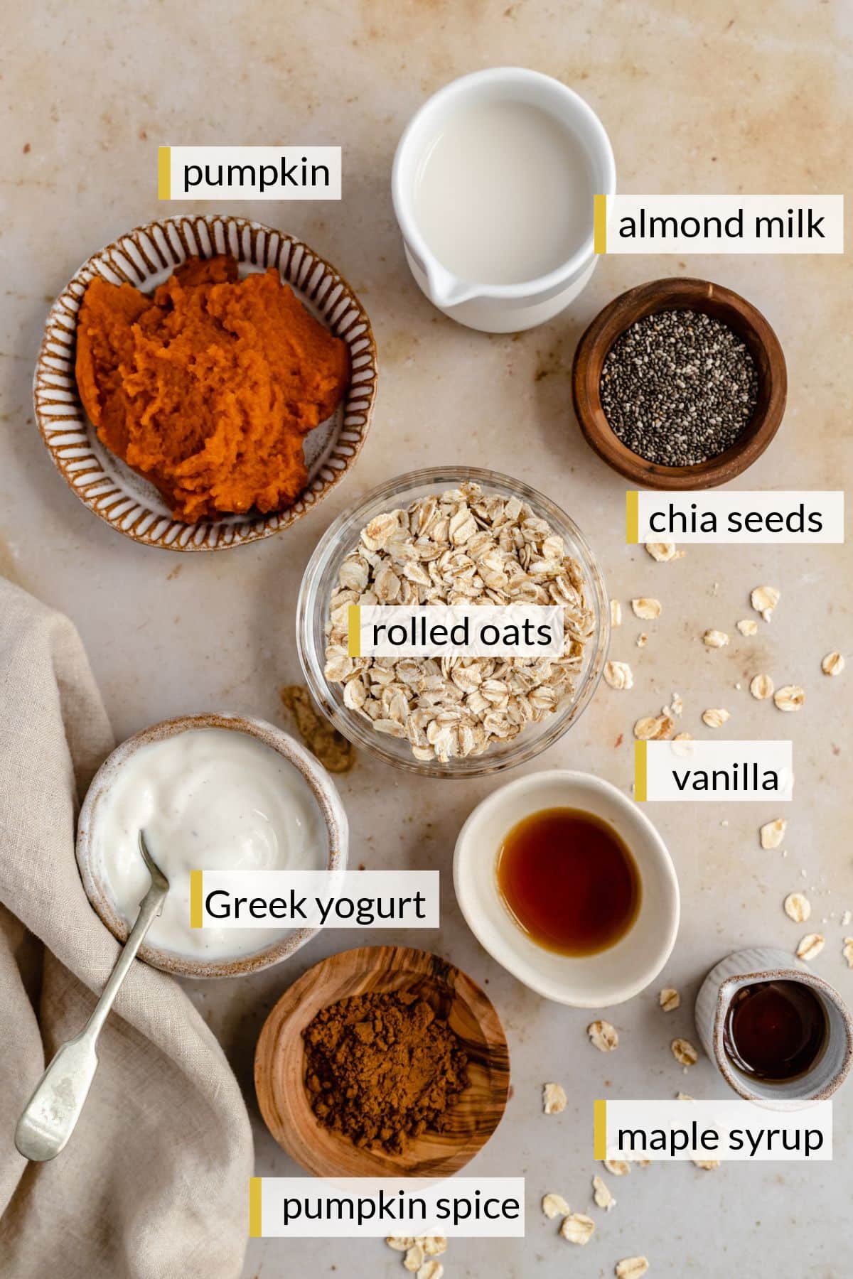 Pumpkin puree, almond milk, oats, greek yogurt, chia seeds and spices divided into small bowls.