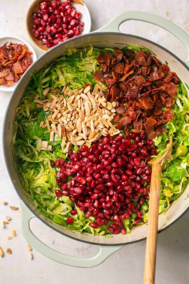 Adding almonds, pomegranate seeds and bacon to cooked vegetables in a pot.