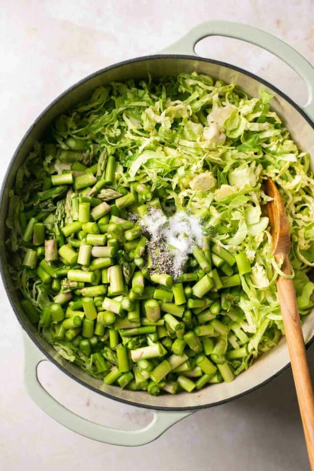 Adding asparagus and shaved brussel sprouts to a pot.