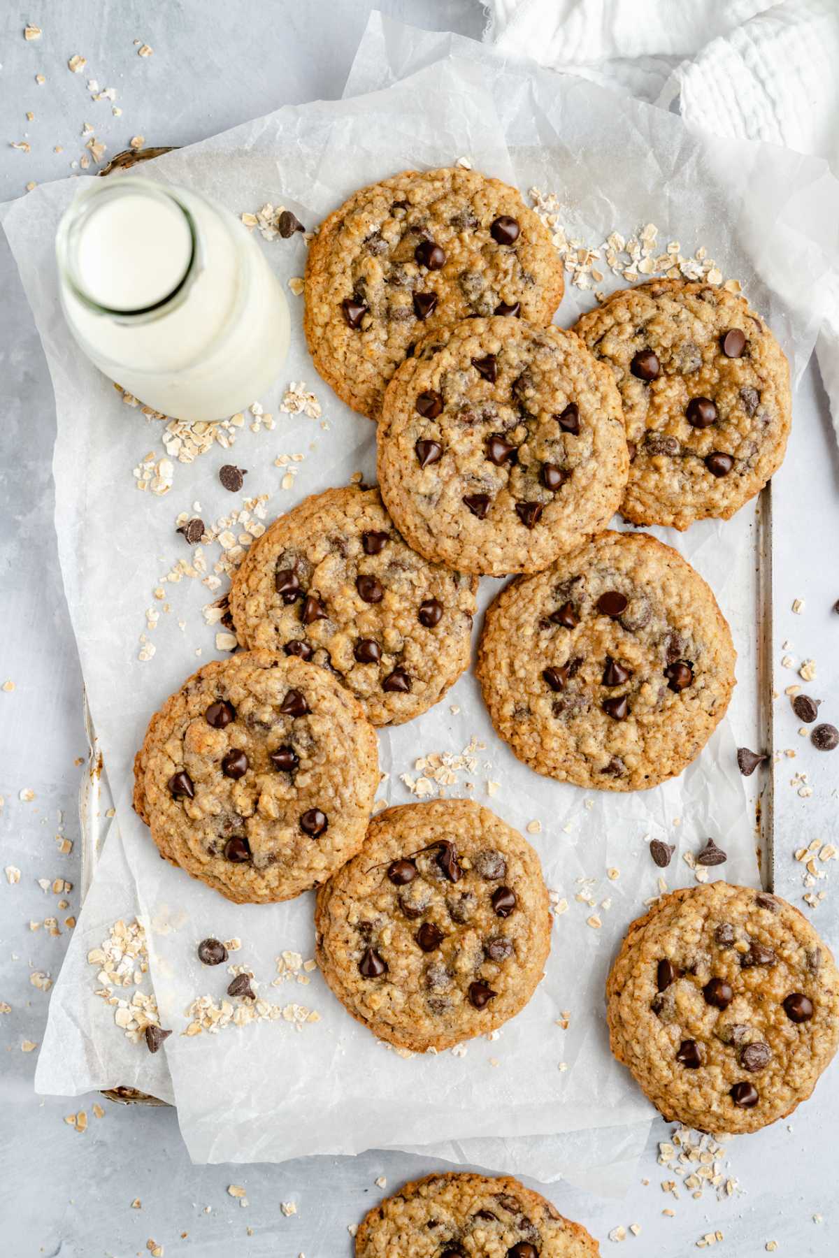 Oatmeal chocolate chip cookies on parchment paper with a glass of milk.