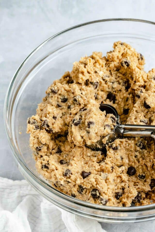 Scooping cookie dough out of a large bowl.