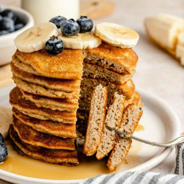 Cutting pancakes topped with bananas and blueberries with a fork.