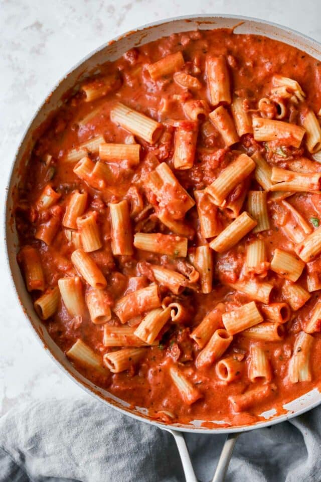 Rigatoni noodles cooking in a creamy red sauce.