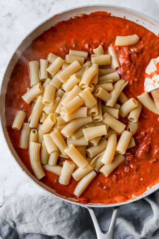 Stirring pasta into tomato sauce.