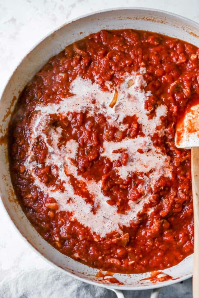Adding half and half to tomato sauce in a skillet.