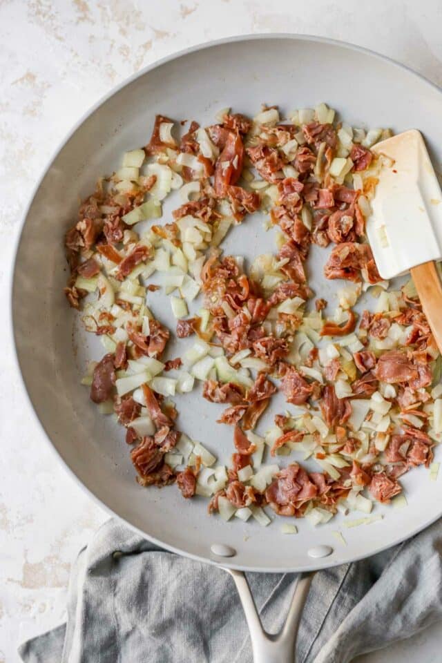 Cooking prosciutto with onion in a skillet.