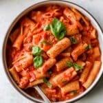 Bowl filled with rigatoni and covered with a creamy tomato pasta sauce.