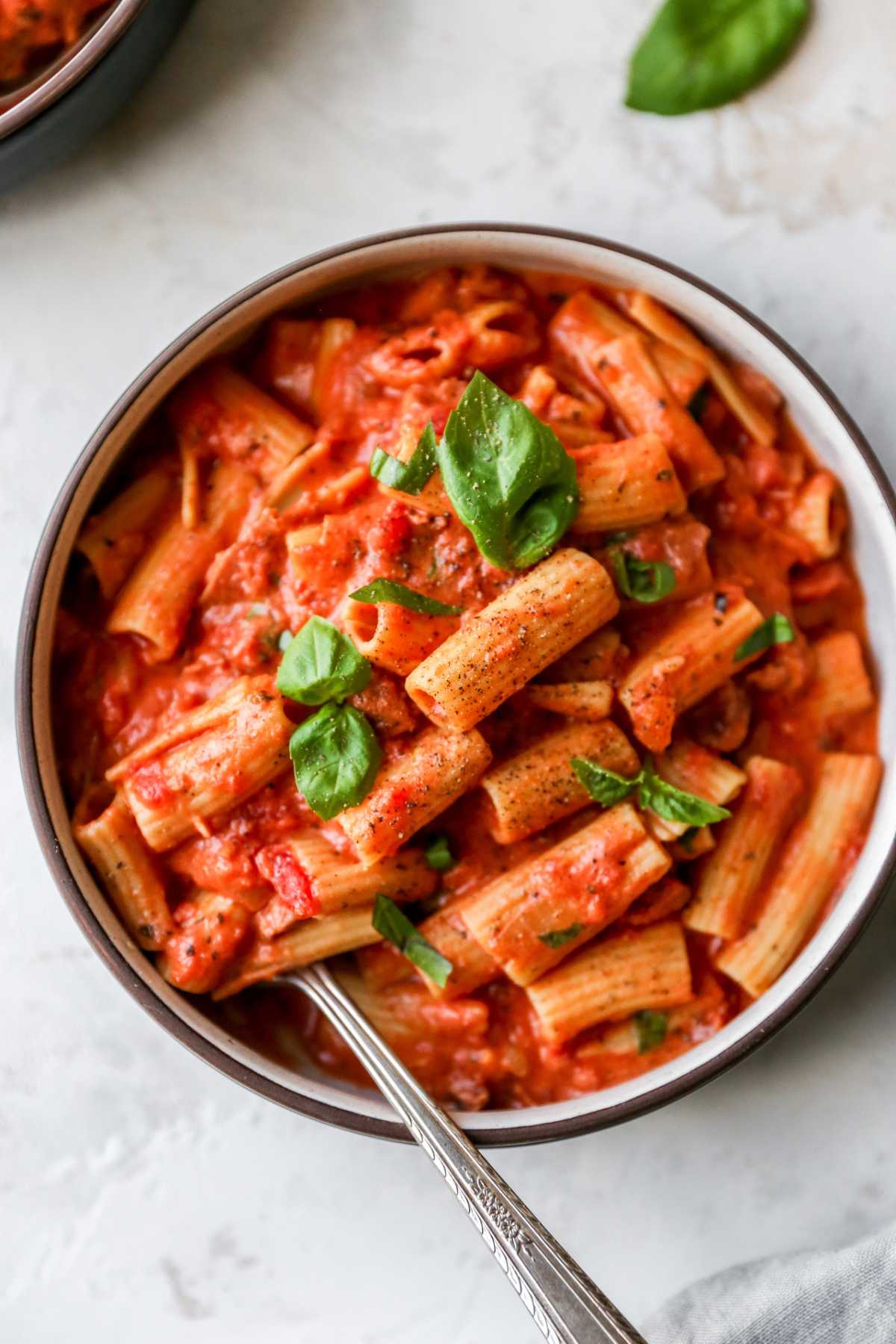Bowl filled with rigatoni and covered with a creamy tomato pasta sauce.