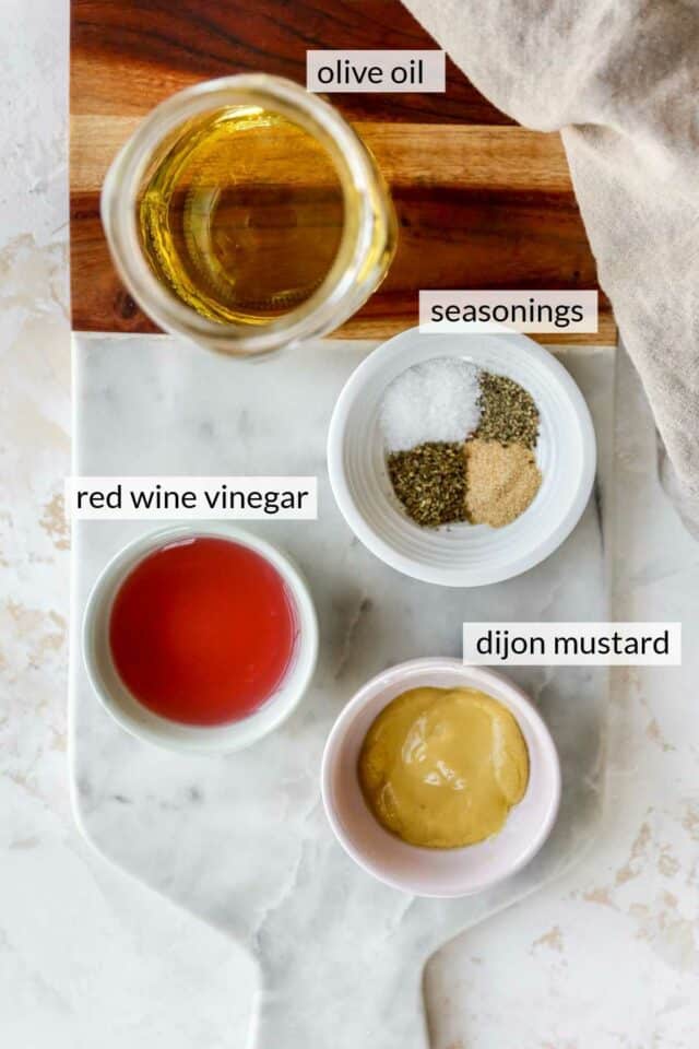 Olive oil, red wine vinegar, dijon mustard and seasonings divided into small bowls.
