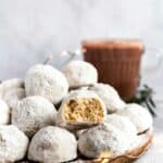 Mexican wedding cookies on a plate with a bite out of one.