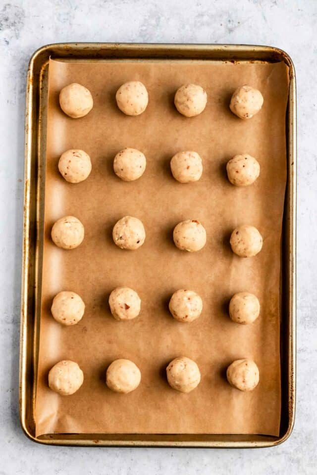Rolled cookie dough balls on a parchment lined sheet pan.