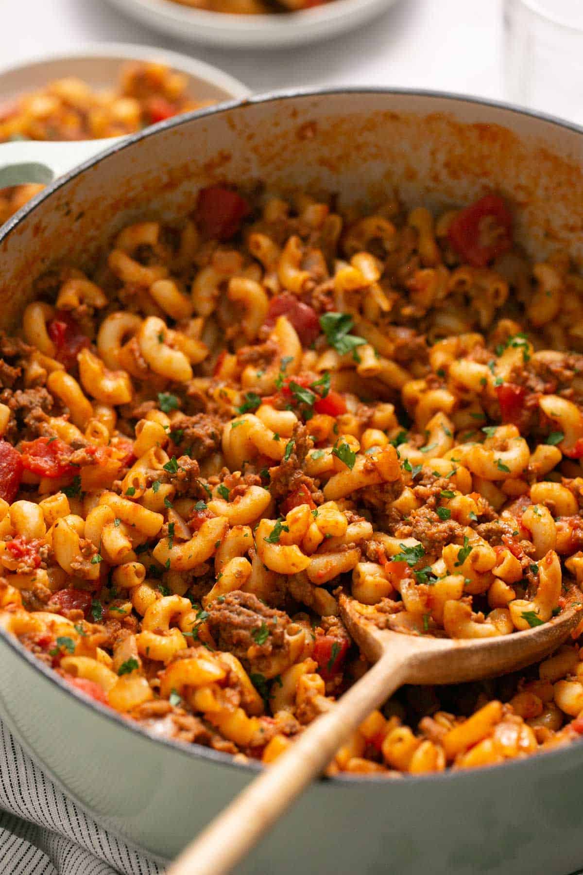 Stirring American Goulash in a Dutch oven with a wooden spoon.