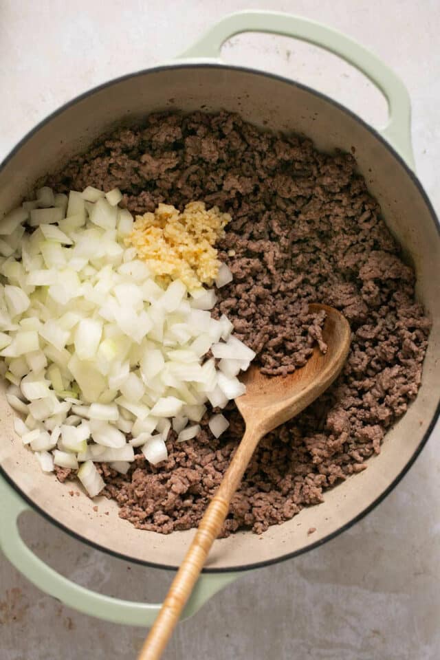 Stirring onion and garlic into browned ground beef.