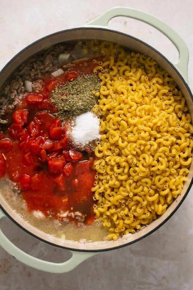 Mixing pasta, seasonings and tomato sauce in with ground beef.