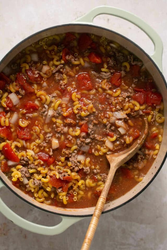 Using a wooden spoon to stir pasta with meat and tomatoes.  