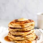 A stack of buttermilk pancakes topped with butter and maple syrup.