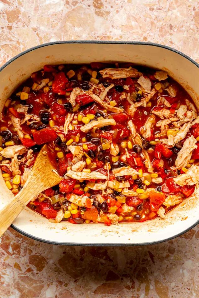 Stirring shredded chicken with diced tomatoes, chicken broth, beans and corn.