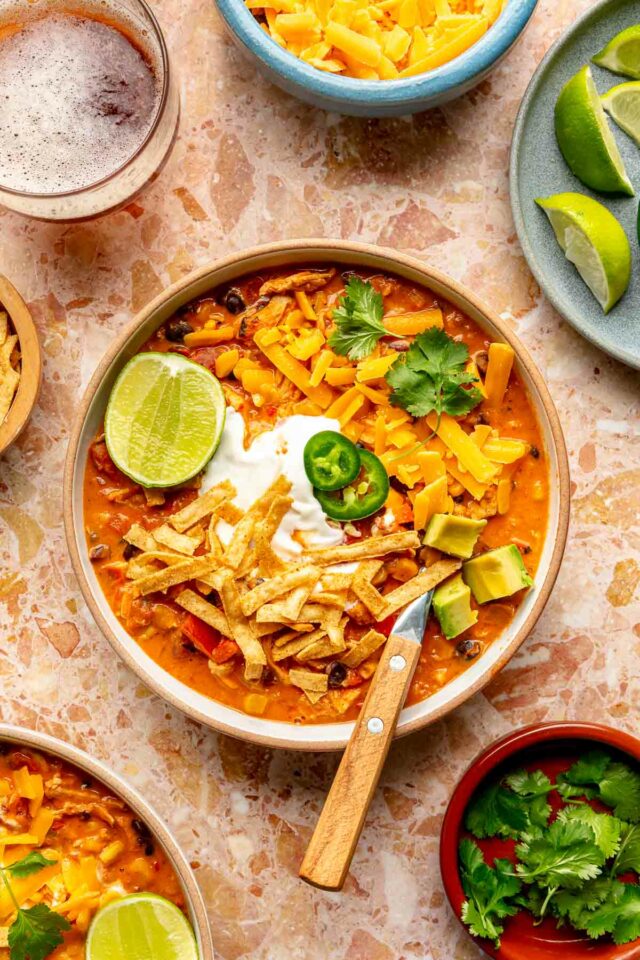 Creamy chicken chili in a bowl with toppings like lime, jalapeños and cilantro.