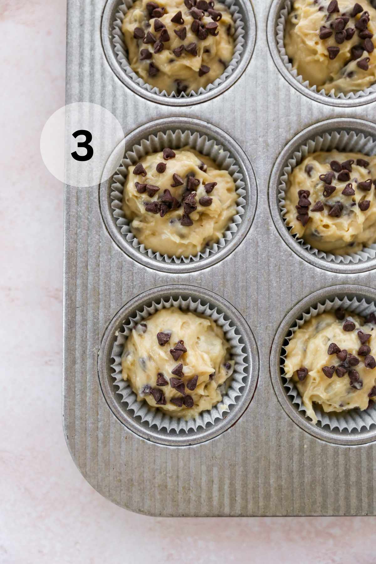 Batter in a muffin pan topped with chocolate chips.