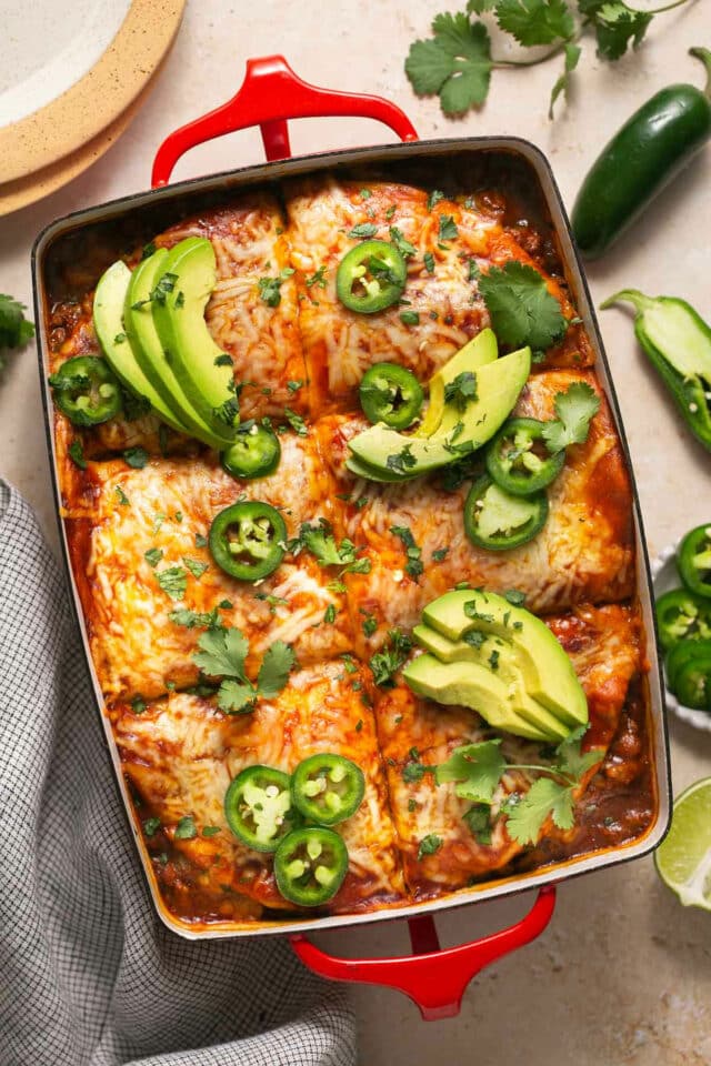 Enchilada casserole in a baking dish and topped with avocado slices and sliced jalapeños.