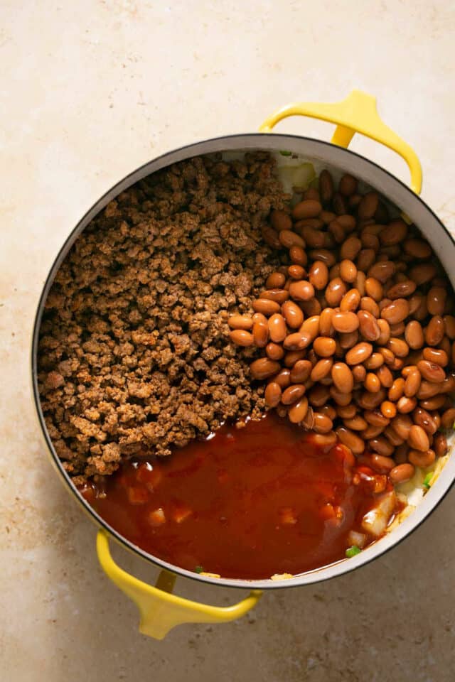 Adding beans and enchilada sauce in a pot with ground meat.
