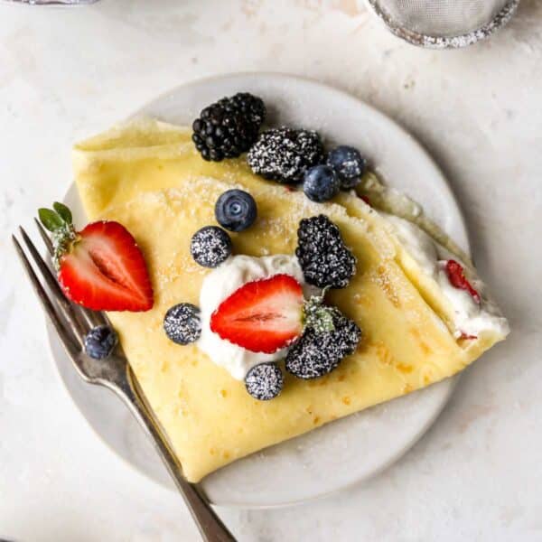 Folded crepe on a white plate, filled with whipped cream and topped with fresh berries.