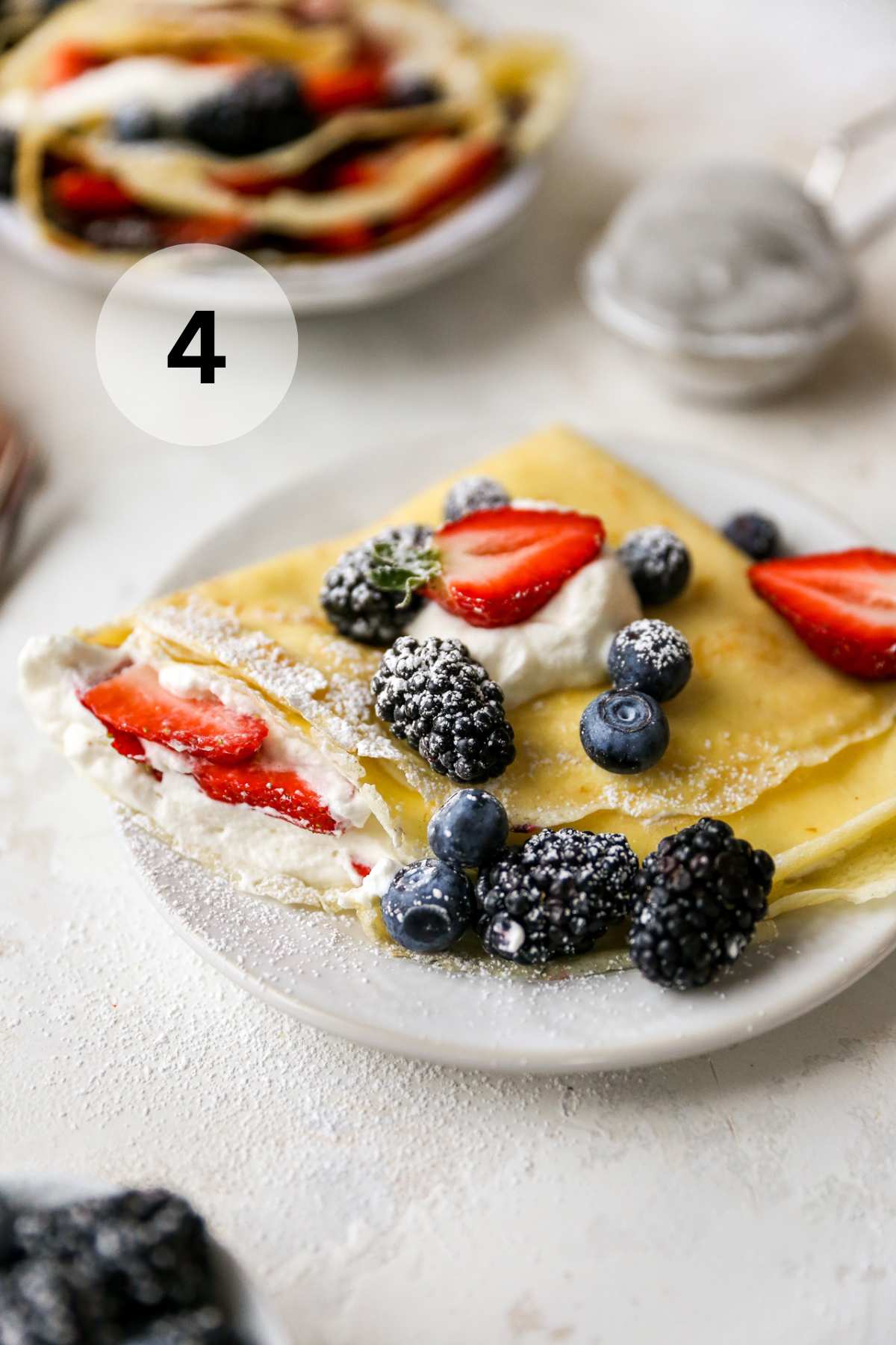 Homemade crepe served on a small white plate with berries and a dusting of powdered sugar.