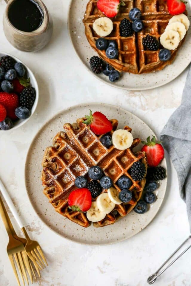 Protein waffle on a plate with a dusting of powdered sugar and fruit.